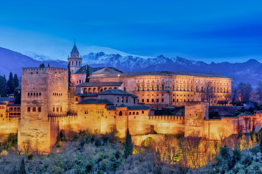Stunning view of the illuminated Alhambra Palace with snowy mountains in Granada.