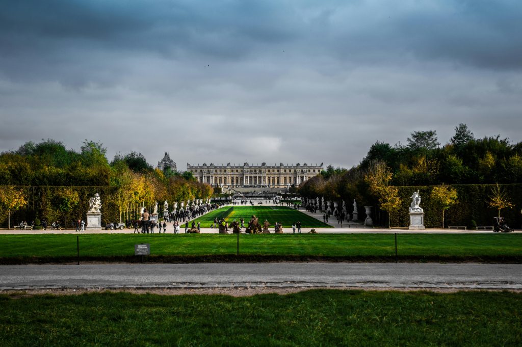 Scenic view of the lush gardens and majestic Palace of Versailles under an overcast sky.