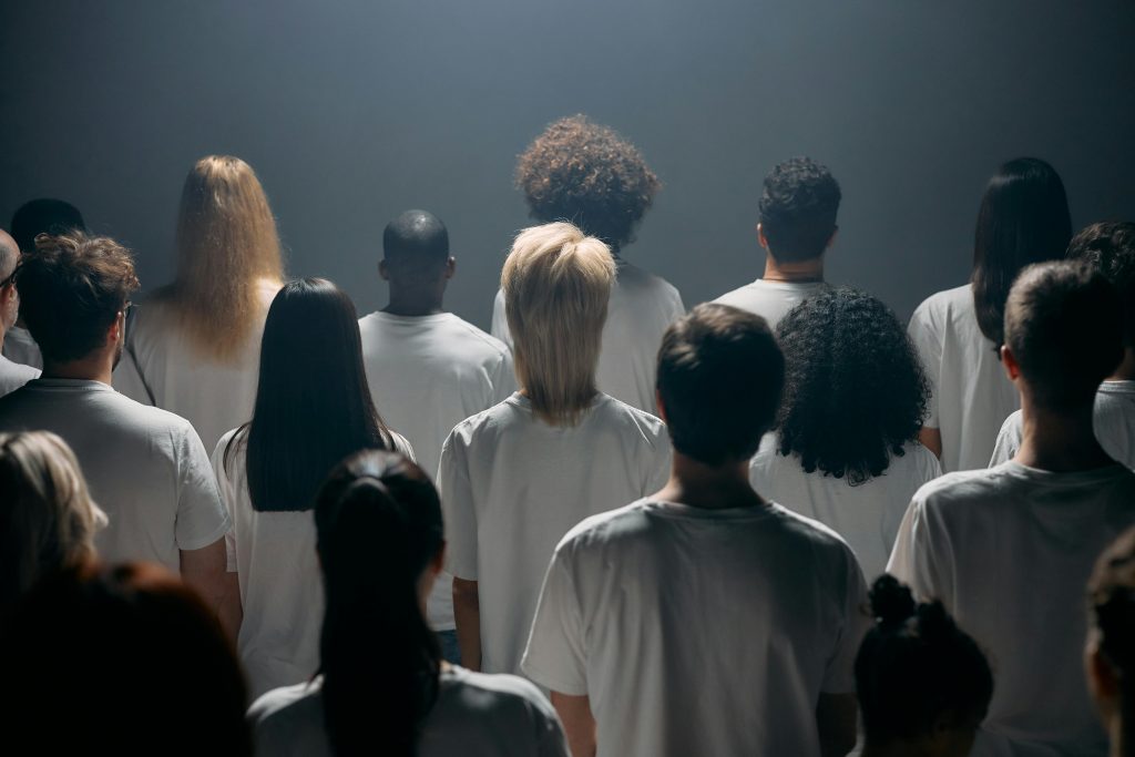 A diverse group of people facing forward in a studio setting wearing white shirts.