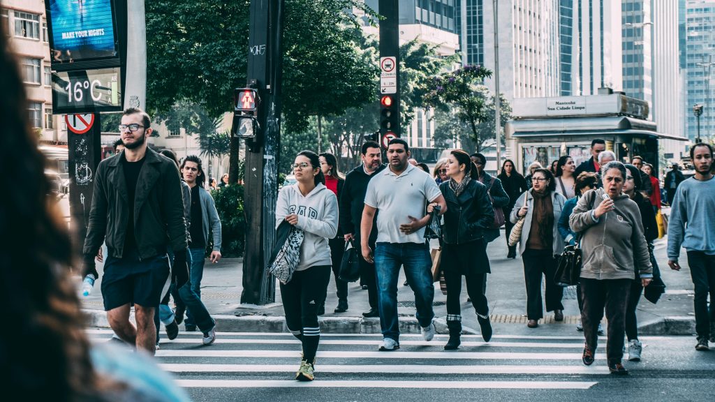A diverse group of people crossing a street in a bustling city setting with skyscrapers.